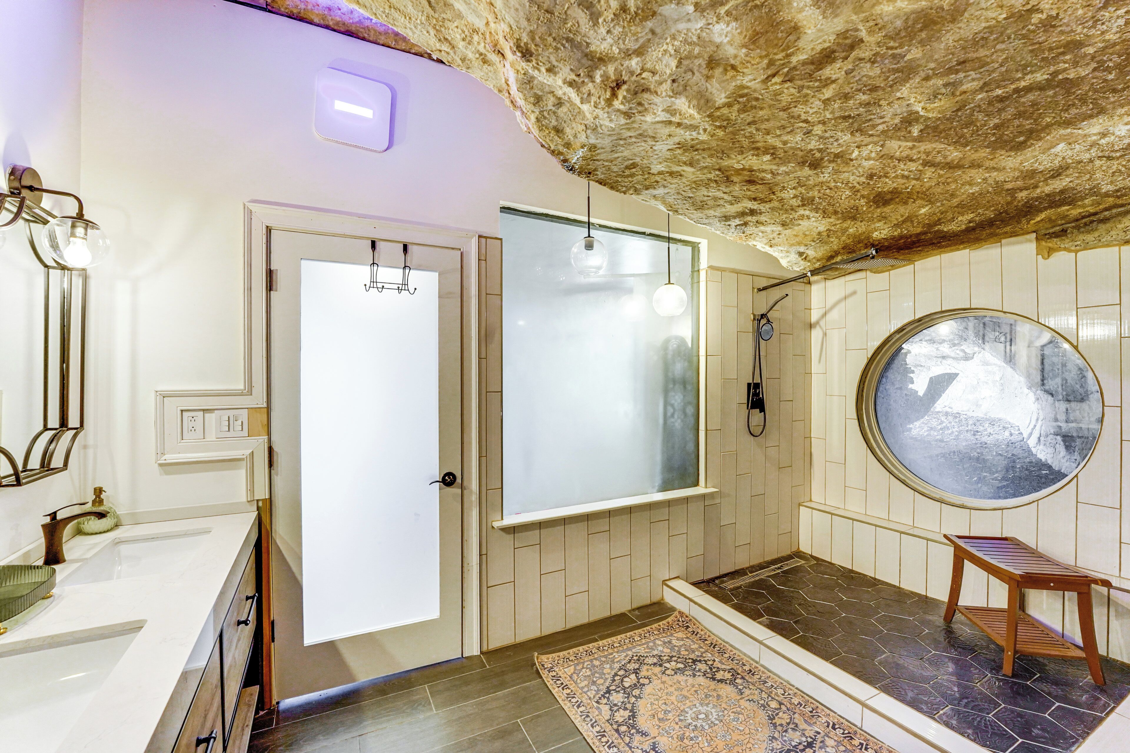 A bathroom with a white sink, a mirror, a towel rack, a shower, and a circular window.