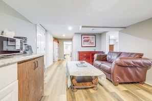 A kitchen with a microwave, coffee maker, and wooden cabinets. There is a dining table with a floral tablecloth and a brown leather couch. A red cabinet and a framed picture are also visible. - Near Southern Regional MC! Commuter-friendly Base (Riverdale)