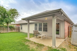 A single-story house with a covered patio, a lawn, and a wooden fence.