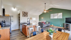 A modern kitchen with a central island, a dining area with a wooden table and chairs, a grey sofa, and a ceiling fan. - 3-unit Combo w/ Dock on Lake Keowee - Hike & Fish! (Seneca)