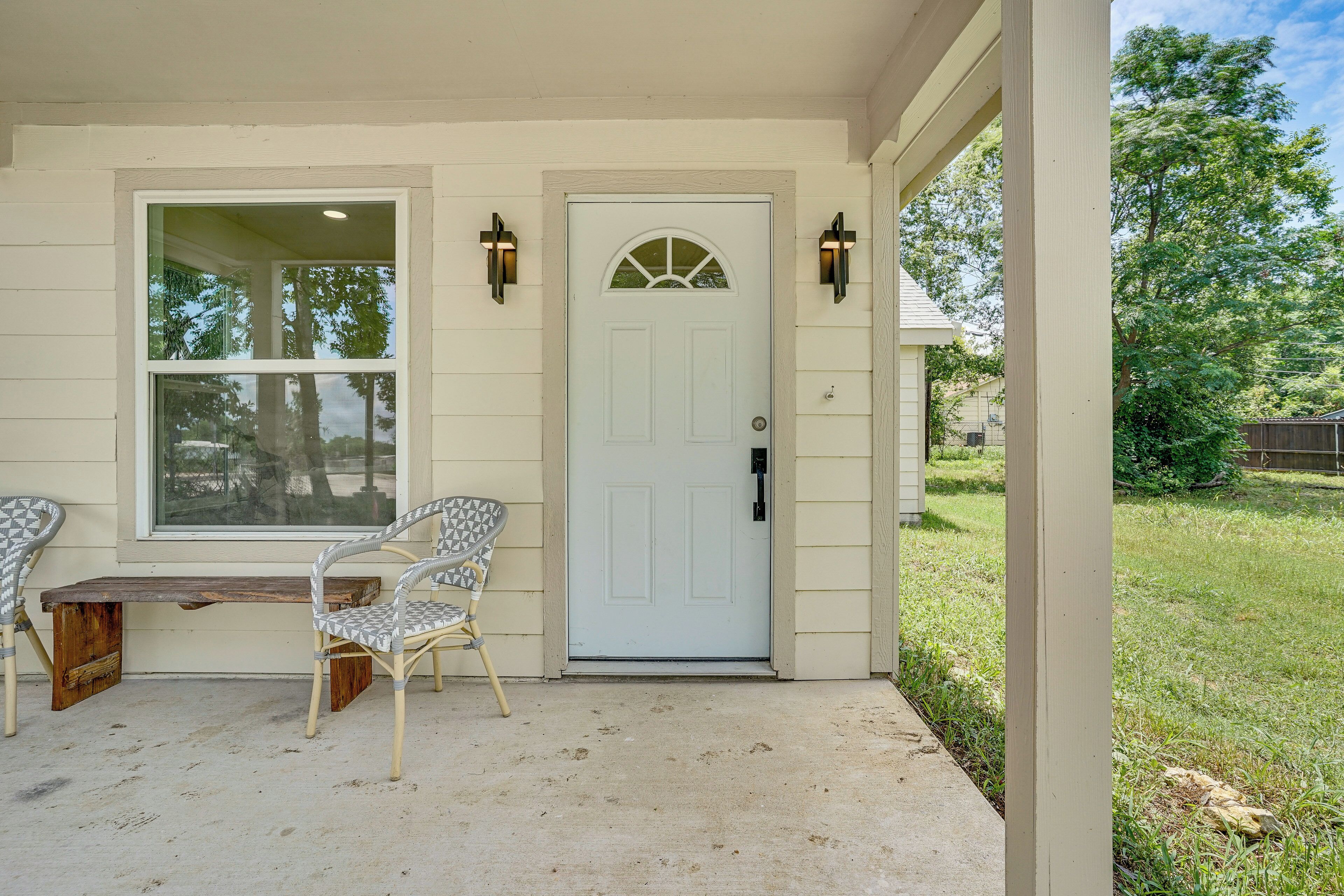 A house with a white door, two wall-mounted lights, a bench, and two chairs outside.