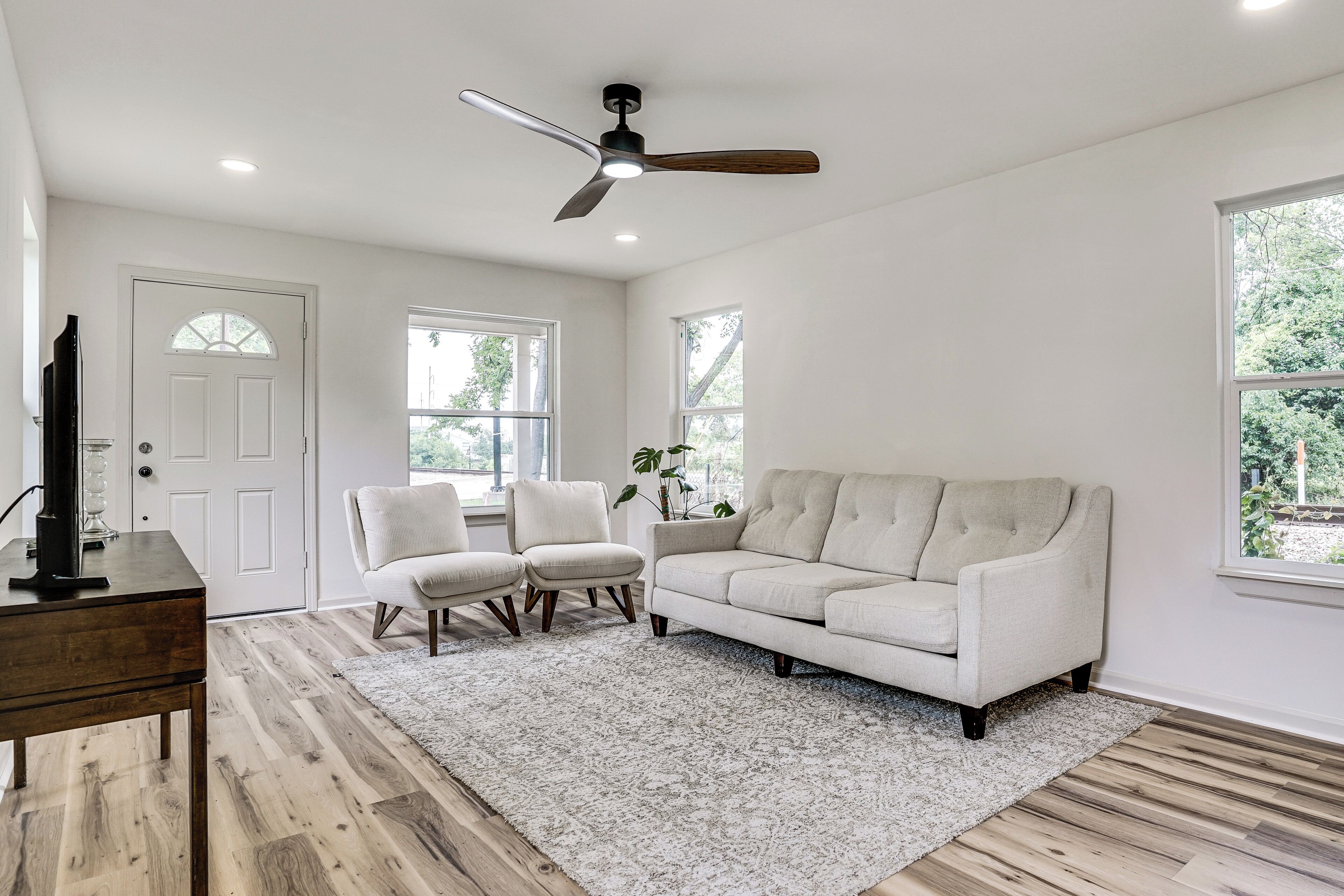 Un salon avec un canapé blanc, deux fauteuils, une table basse en bois et un ventilateur de plafond.