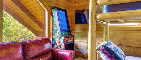 A wooden cabin interior with a red leather couch, bunk beds, and a video game console.