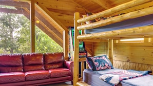 A cabin with a bunk bed, a red leather sofa, and a window overlooking greenery. - Smoky Mtn Oasis w/ Hot Tub! 5 Mi to Skyland Ranch (Sevierville)