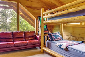 Eine Hütte mit einem Etagenbett, einem roten Ledersofa und einem Fenster mit Blick auf Grünflächen.