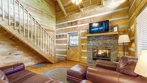 A log cabin interior with a fireplace, leather furniture, a staircase, and a television. - Smoky Mtn Oasis w/ Hot Tub! 5 Mi to Skyland Ranch (Sevierville)
