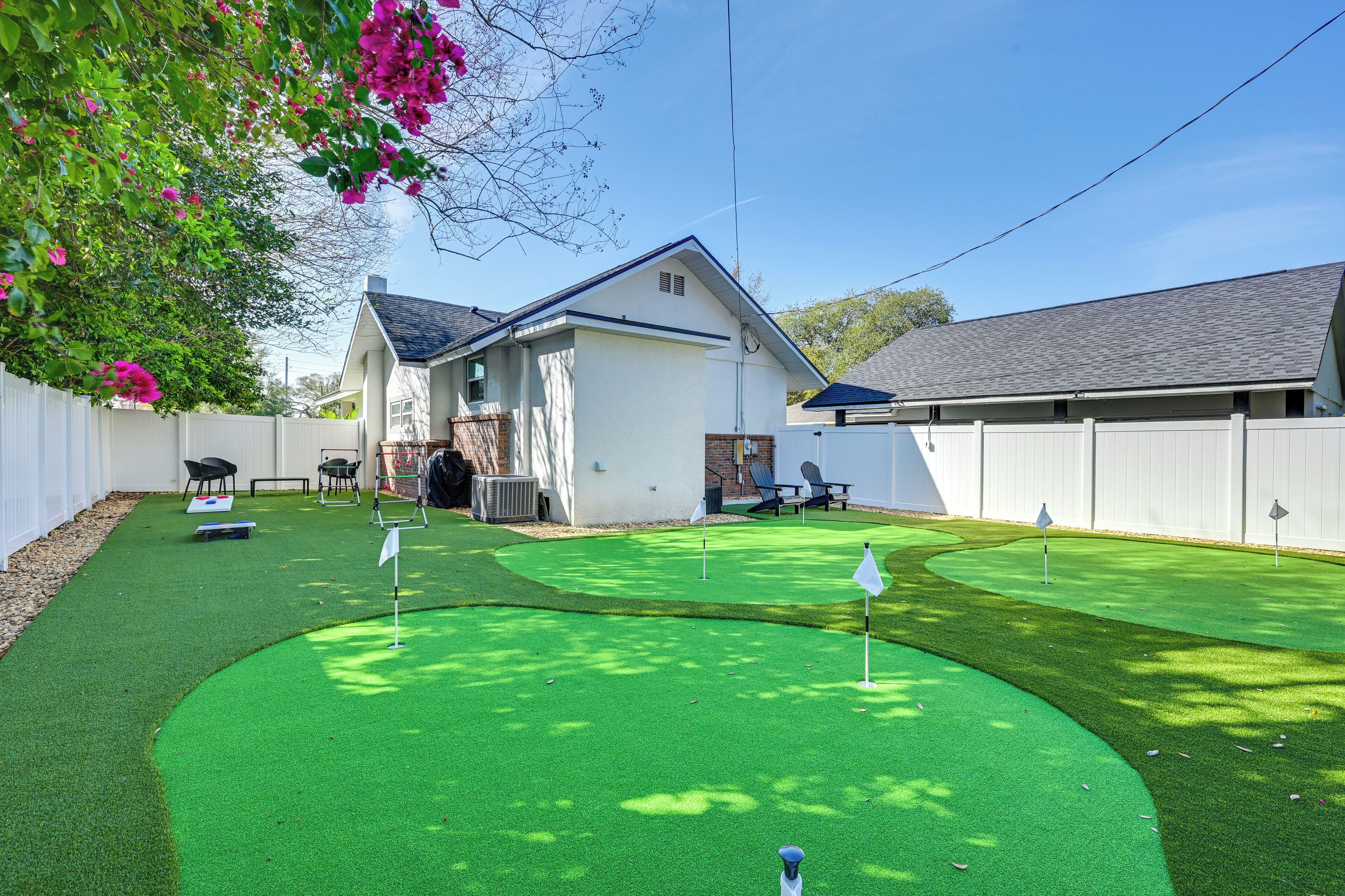 Un patio trasero con césped artificial verde, una valla blanca y una casa con techo gris.