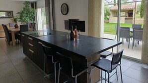 Una cucina moderna con una grande isola, sgabelli da bar, un'area pranzo con sedie, una pianta in vaso e vista sul patio esterno.