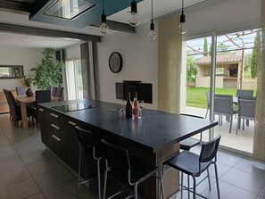 A modern kitchen with a large island, bar stools, a dining area with chairs, a potted plant, and a view of the outdoor patio. - House in the heart of a vineyard in Provence at the foot of Mont Ventoux (Carpentras)