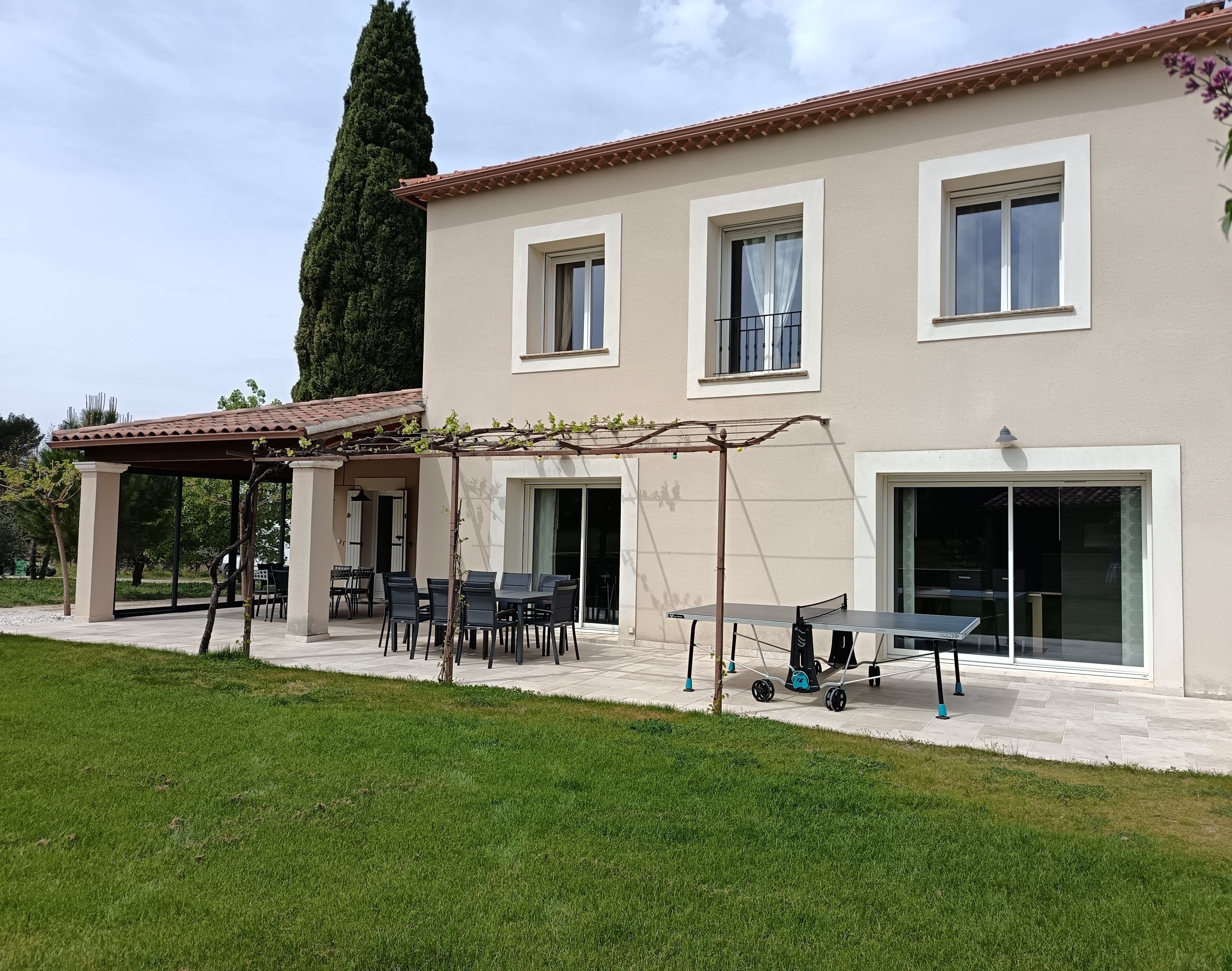 A two-story house with a patio, a pergola, a table, and chairs.