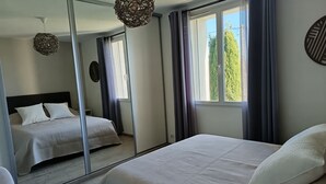 Una camera da letto con un grande specchio, due letti, una lampada a sospensione e una finestra con tende.
