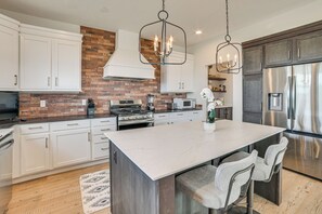 Cozinha moderna com armários brancos, parede de tijolos, eletrodomésticos de aço inoxidável e bancada de mármore.
