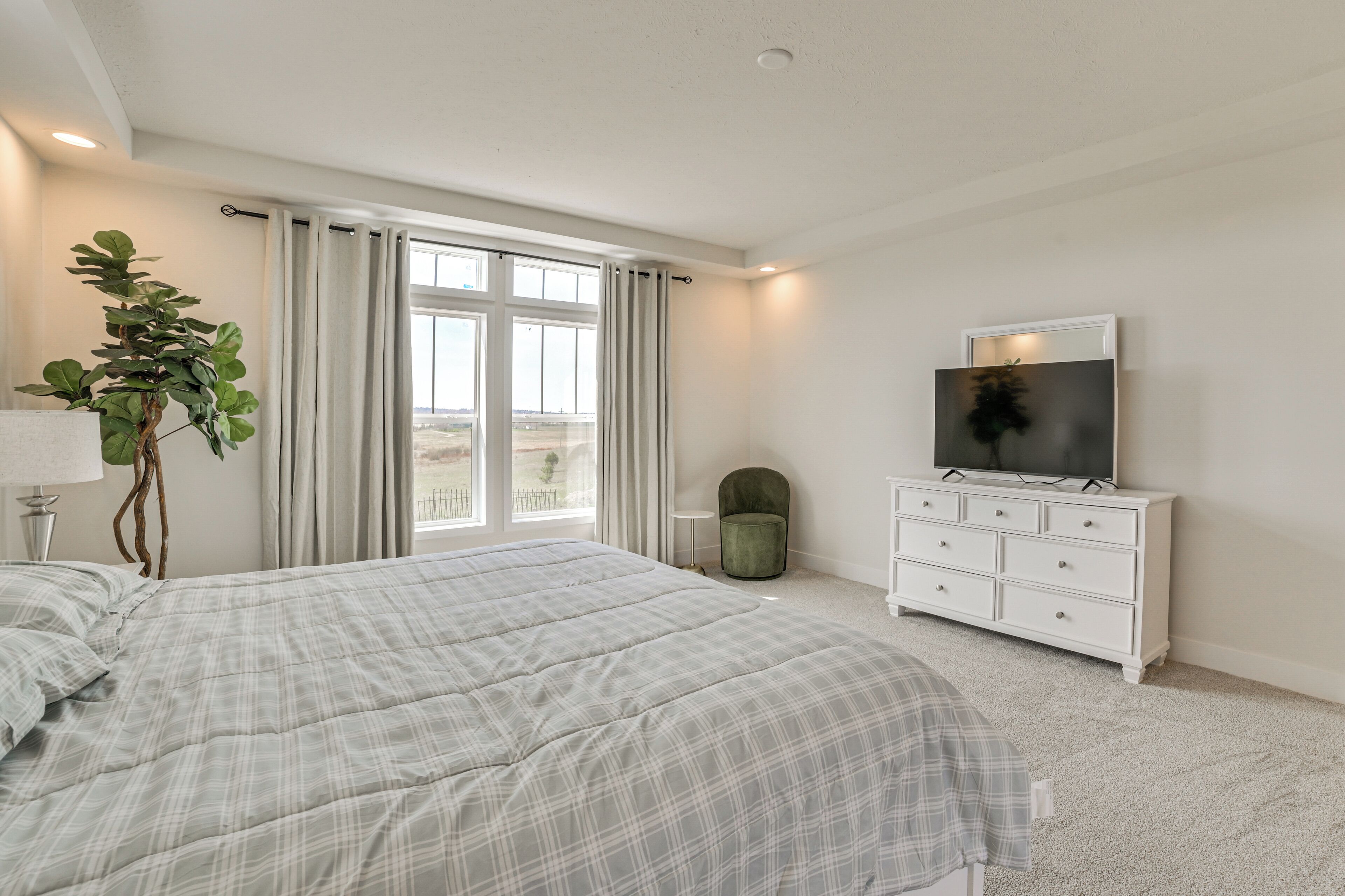 A bedroom with a bed, a TV on a dresser, a plant, and a window with curtains.