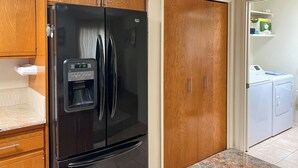 A kitchen with a black refrigerator, wooden cabinets, a marble countertop, and a laundry area with a washing machine. - Mountain View! 55-plus Green Valley Townhome (Green Valley)