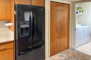 Una cocina con un refrigerador negro, armarios de madera, encimera de mármol y un área de lavandería con lavadora.