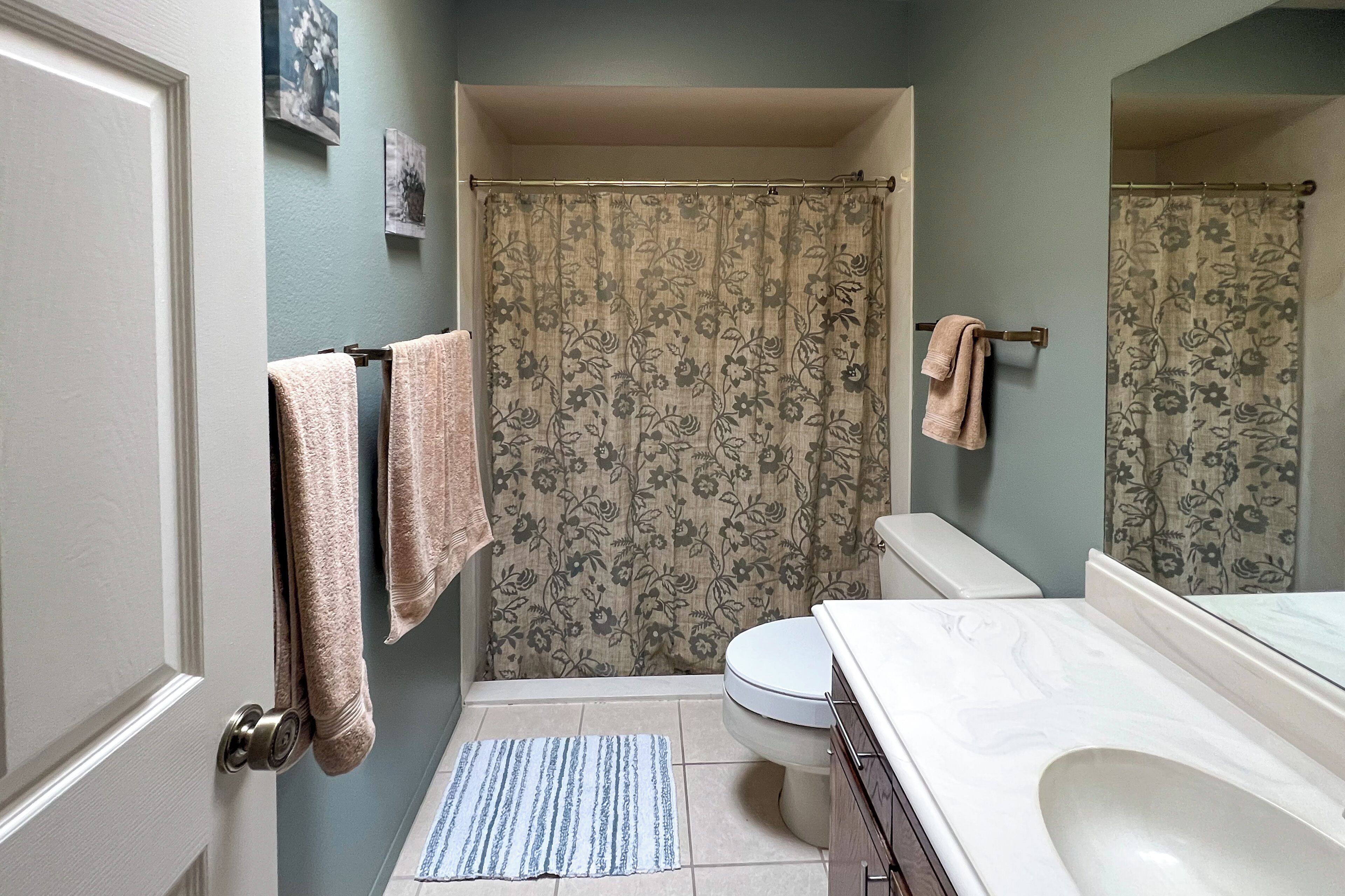 A bathroom with a shower curtain, a toilet, a sink, and a mirror.