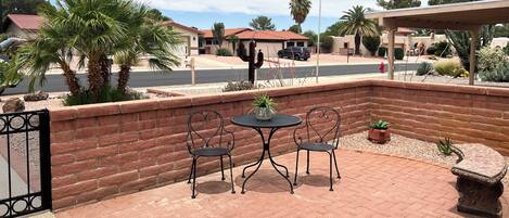 A patio with two metal chairs and a table, surrounded by a brick wall and various plants.