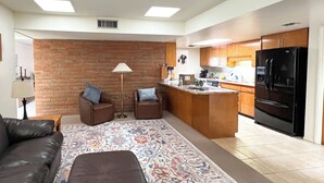 A modern living room with a brown leather sofa, two armchairs, a patterned rug, and a kitchen area with wooden cabinets and a black refrigerator. - Mountain View! 55-plus Green Valley Townhome (Green Valley)
