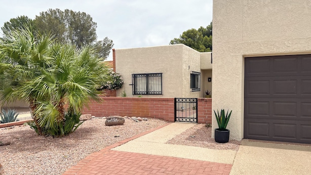 A residential property with a paved driveway, a palm tree, a brick wall, a garage door, and a gate. - Mountain View! 55-plus Green Valley Townhome (Green Valley)