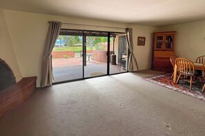 Ein Zimmer mit einer Schiebeglastür, die auf eine Terrasse im Freien führt, einem Holzschrank und einem Esstisch mit Stühlen.