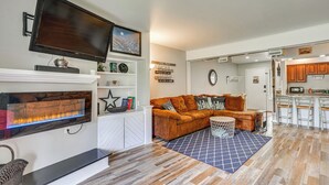 Sala de estar con chimenea, televisor, sofá y una zona de cocina con taburetes de bar.