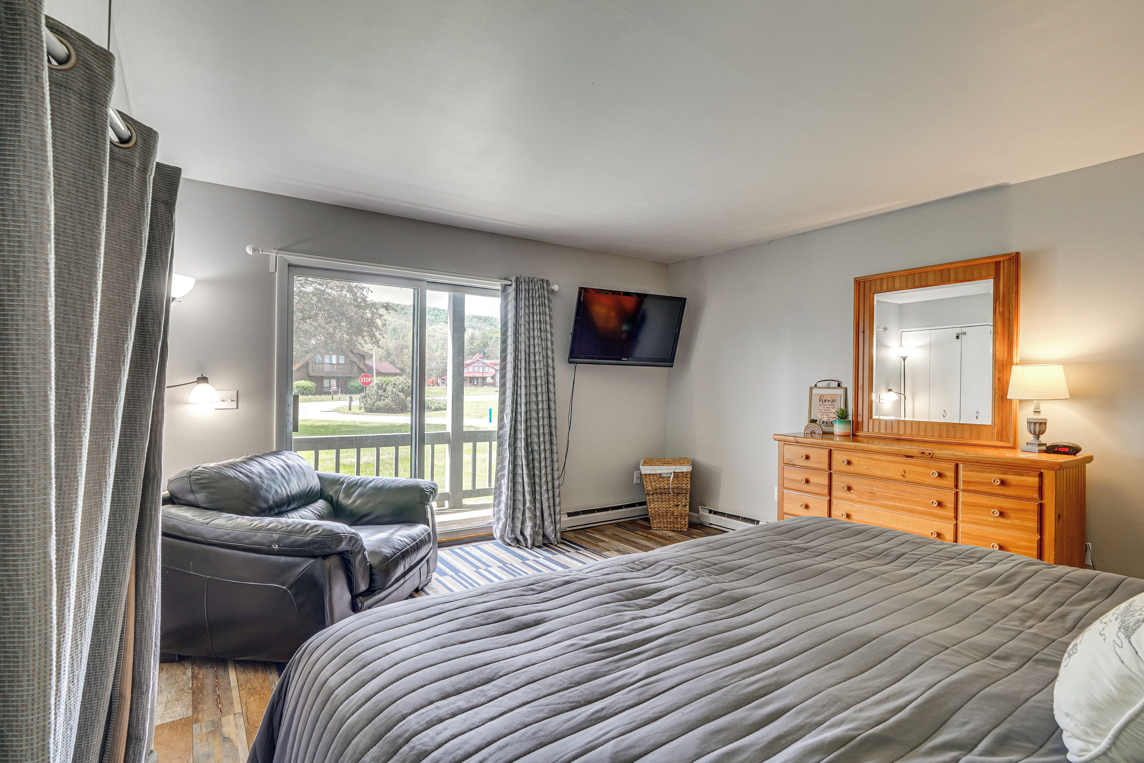 A bedroom with a bed, a dresser, a television, and a view of the outdoors.