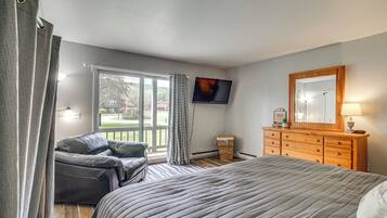 A bedroom with a bed, a dresser, a television, and a view of the outdoors.