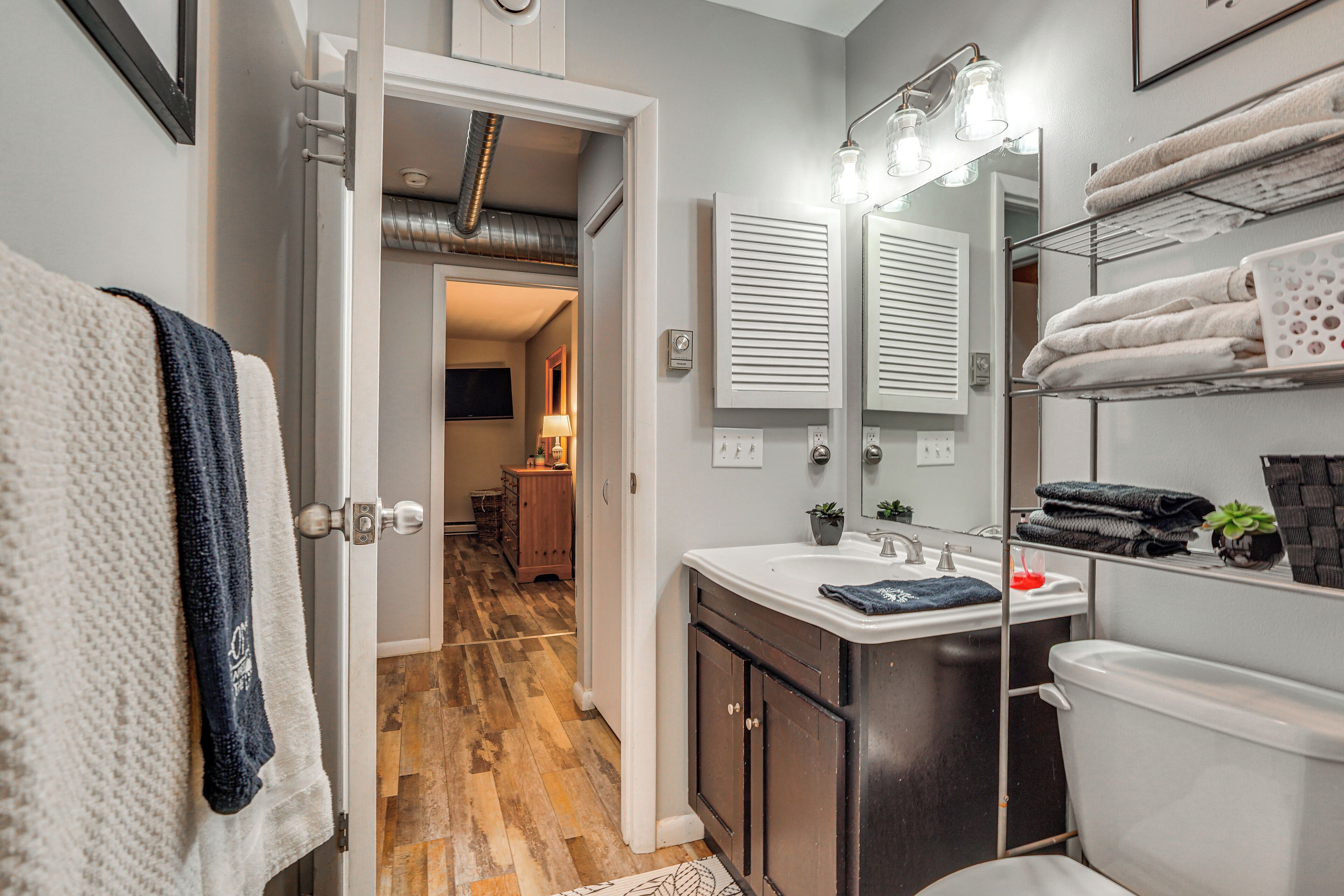 A bathroom with a sink, mirror, towel rack, and a visible door leading to another room.