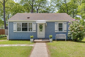 A single-story house with a front porch, a small garden, and a wooden bench.