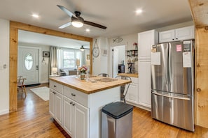 A kitchen with wooden flooring, white cabinets, a stainless steel refrigerator, and a ceiling fan.