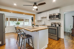 Una cocina moderna con una isla central, taburetes de bar, refrigerador, microondas, horno y ventilador de techo.