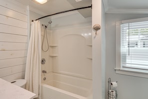 A bathroom with a shower, toilet, and a window with blinds.
