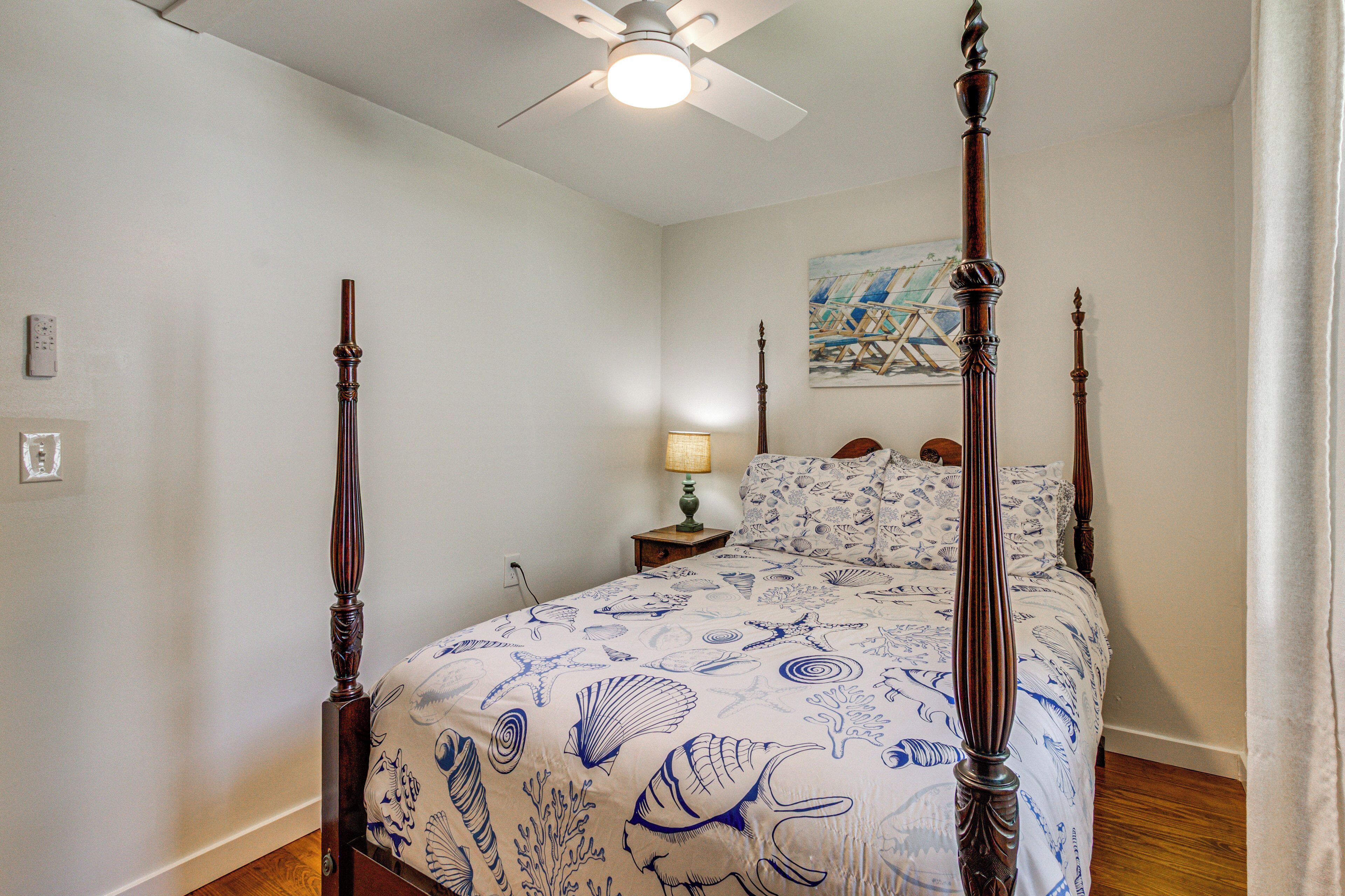 A four-poster bed with a nautical-themed bedspread, a ceiling fan, and a nightstand with a lamp.