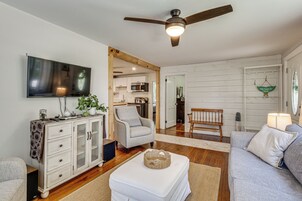 Una sala de estar con televisor, ventilador de techo, sofá, sillón y cocina al fondo.