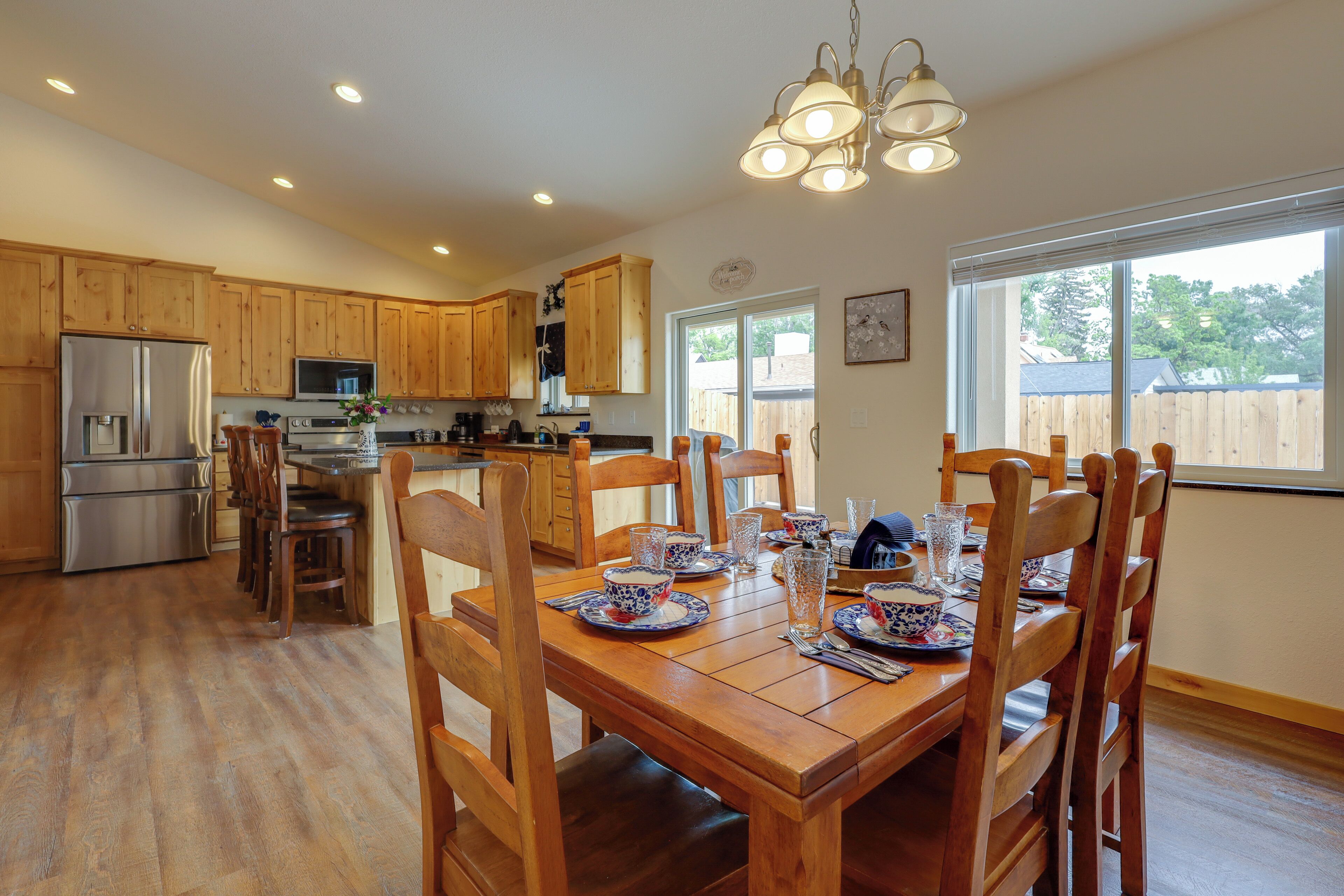 A kitchen with wooden cabinets, a dining table set for six, and a large window.