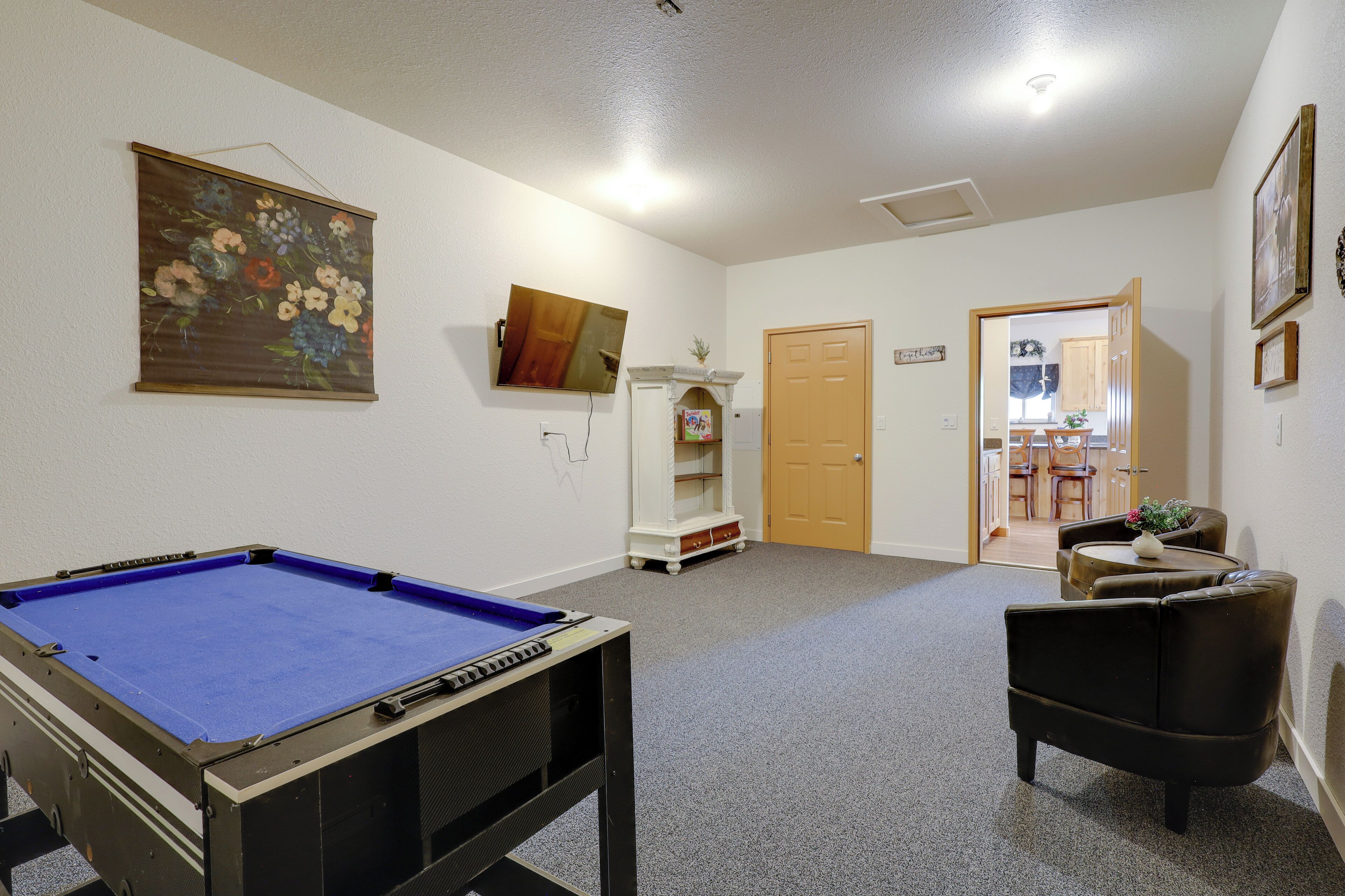 A room with a pool table, a sofa, a door leading to a dining area, and a painting on the wall.