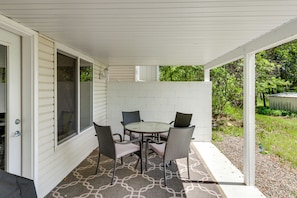 A covered patio with a table and chairs, a door, and a view of the yard.