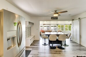 A modern kitchen with a stainless steel refrigerator, a dining area with a wooden table and four chairs, and a ceiling fan.