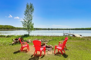 Une vue sur le lac avec trois chaises rouges, un arbre et une jetĂ©e qui sâavance dans lâeau.