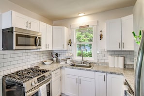 A kitchen with white cabinets, a stainless steel stove, a microwave, and a window with a view of greenery.