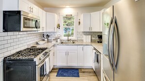 Una cocina moderna con armarios blancos, electrodomésticos de acero inoxidable, una alfombra azul y una ventana con vistas a zonas verdes.