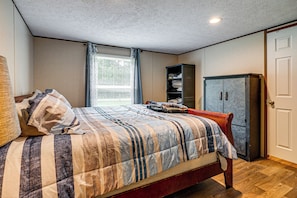 Ein Schlafzimmer mit Bett, Kleiderschrank, Fenster mit Vorhängen und Deckenlampe.