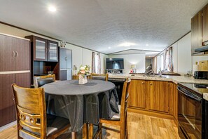 Une cuisine avec des meubles de rangement en bois, une table à manger avec des chaises, un four encastré et un four à micro-ondes.