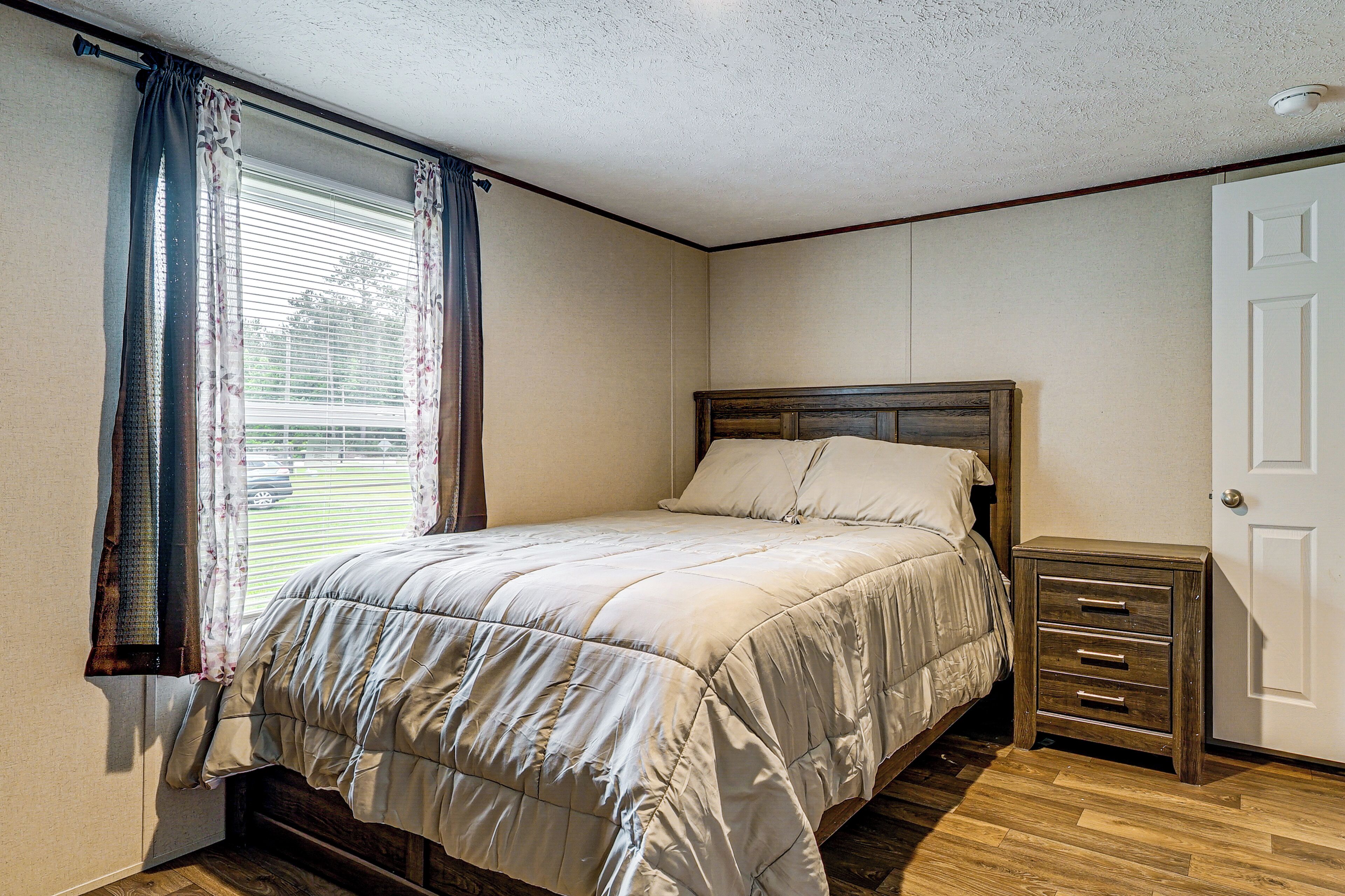 A bedroom with a bed, a nightstand, a door, and a window with curtains.