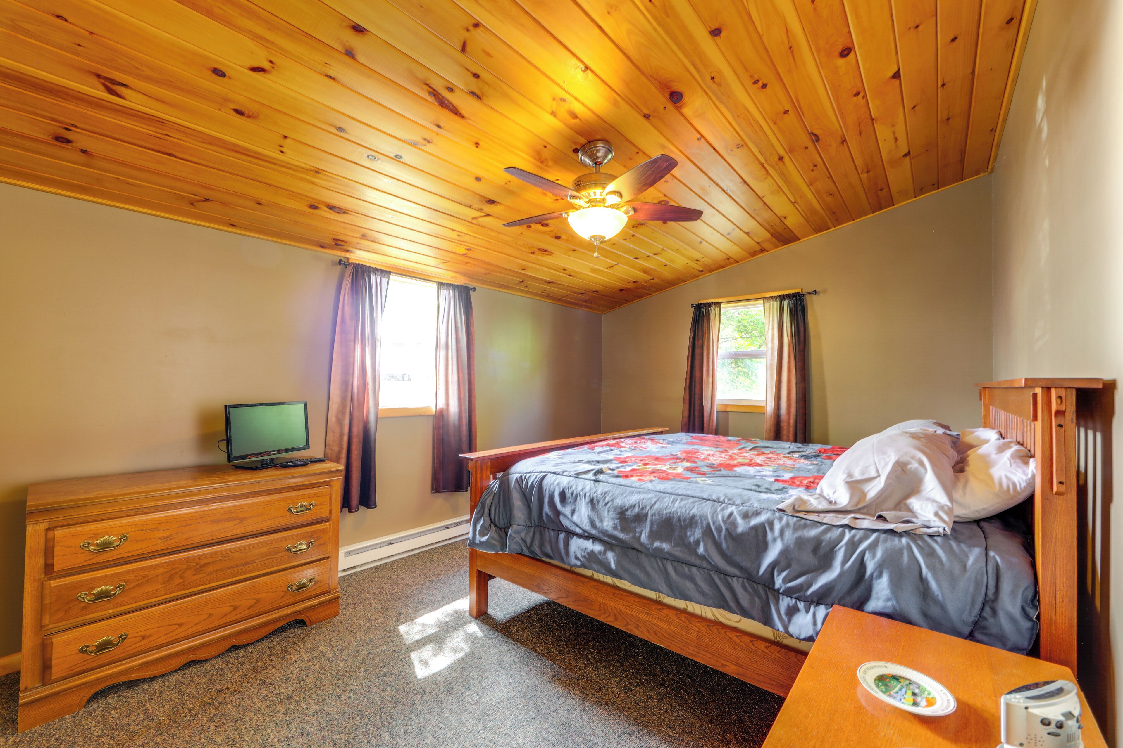Un dormitorio con techo de madera, una cama con colcha azul, un aparador de madera y un televisor sobre él.