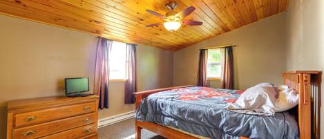 Un dormitorio con techo de madera, una cama con colcha azul, un aparador de madera y un televisor sobre él.