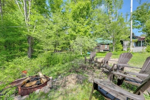 A rustic outdoor setting with a fire pit, Adirondack chairs, and a cabin in the background.