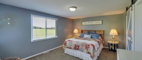 A bedroom with a bed, two bedside lamps, a window with blinds, a chair, and a wall decoration.