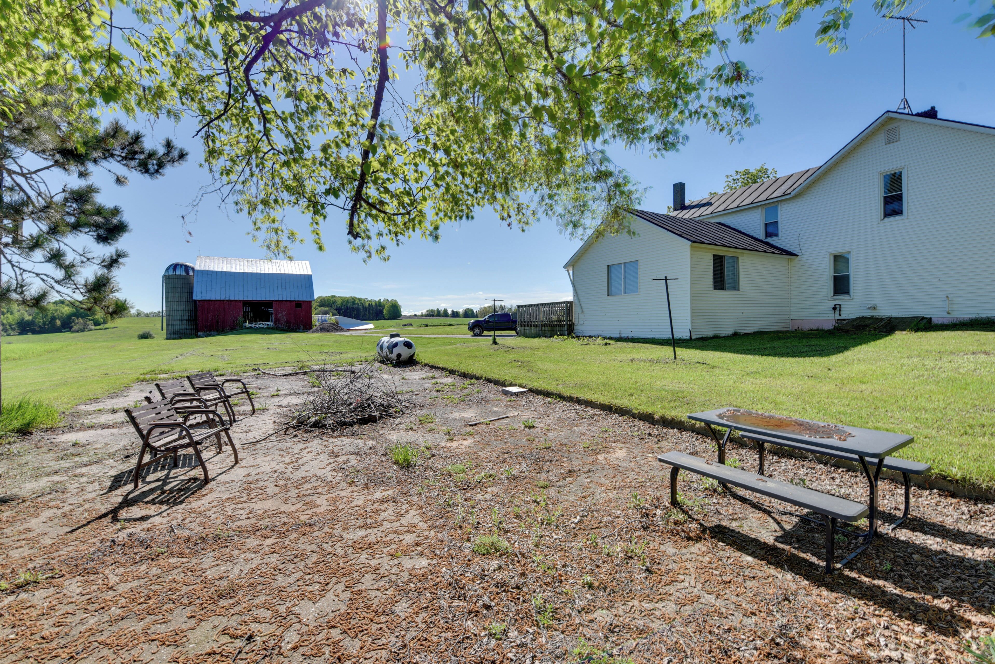 A picnic area with benches and a table, a barn, and a house in a rural setting.