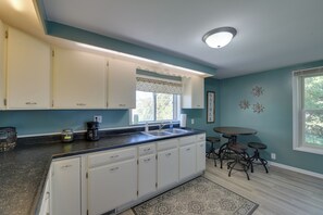 A kitchen with white cabinets, a double sink, a coffee maker, and a window with a patterned valance. - 3 Miles to Torch Lake! Farmhouse w/ Vineyard View (Central Lake)